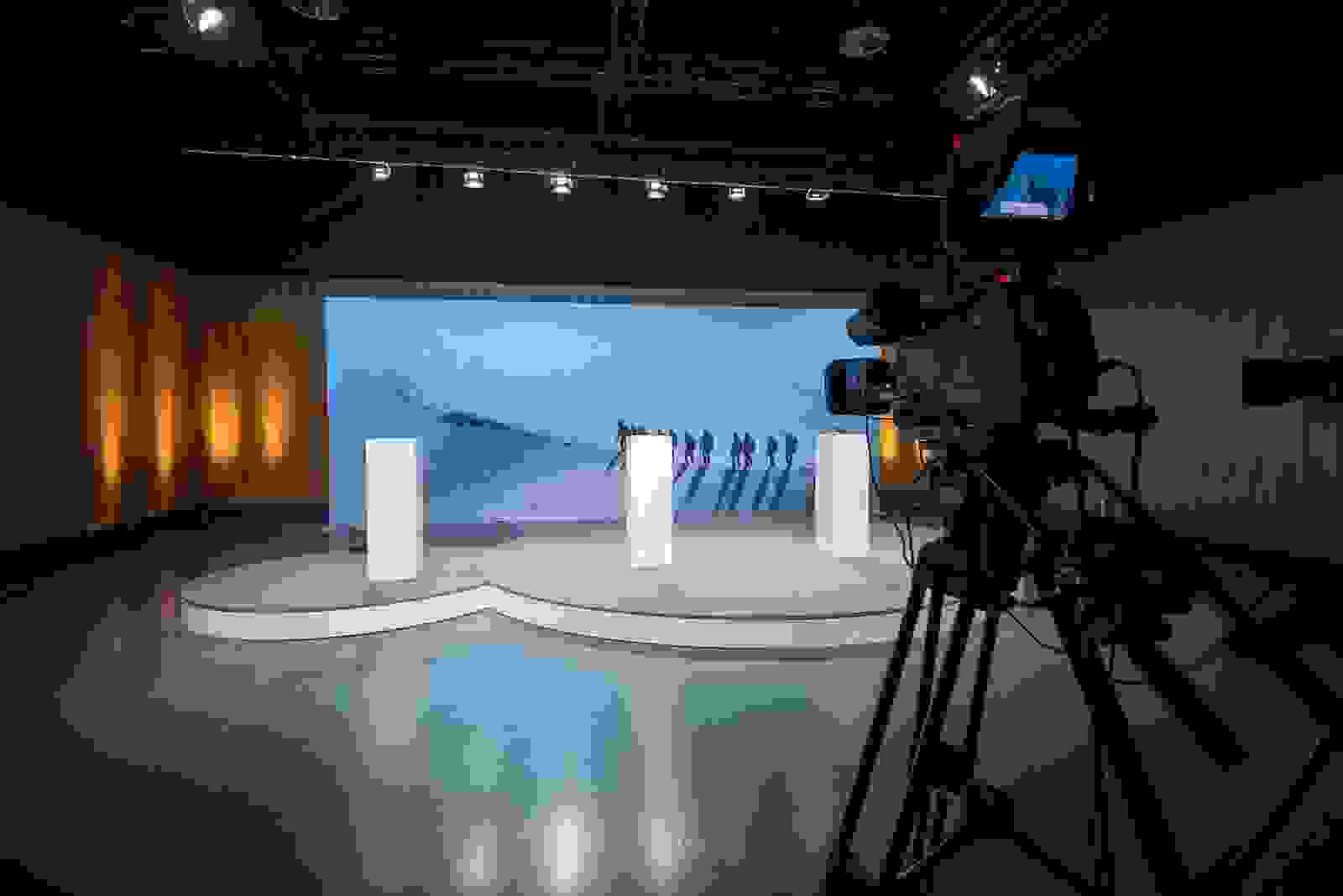 Podium mit grosser Leinwand im Hintergrund. Vordergrund steht eine Kamera, die die digitale Mitarbeiterinformation aufzeichnet. 