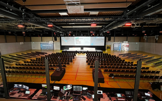 Die Turnhalle mit dem Podizum, grosser Leinwand und Stühlen, Aufnahme von hinten 