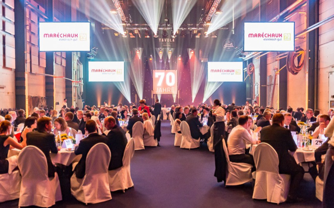 Gäste sitzen an den feierlich dekorierten runden Tischen in der Werfthalle.