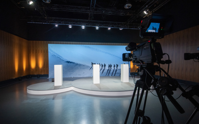 Podium mit grosser Leinwand im Hintergrund. Vordergrund steht eine Kamera, die die digitale Mitarbeiterinformation aufzeichnet. 