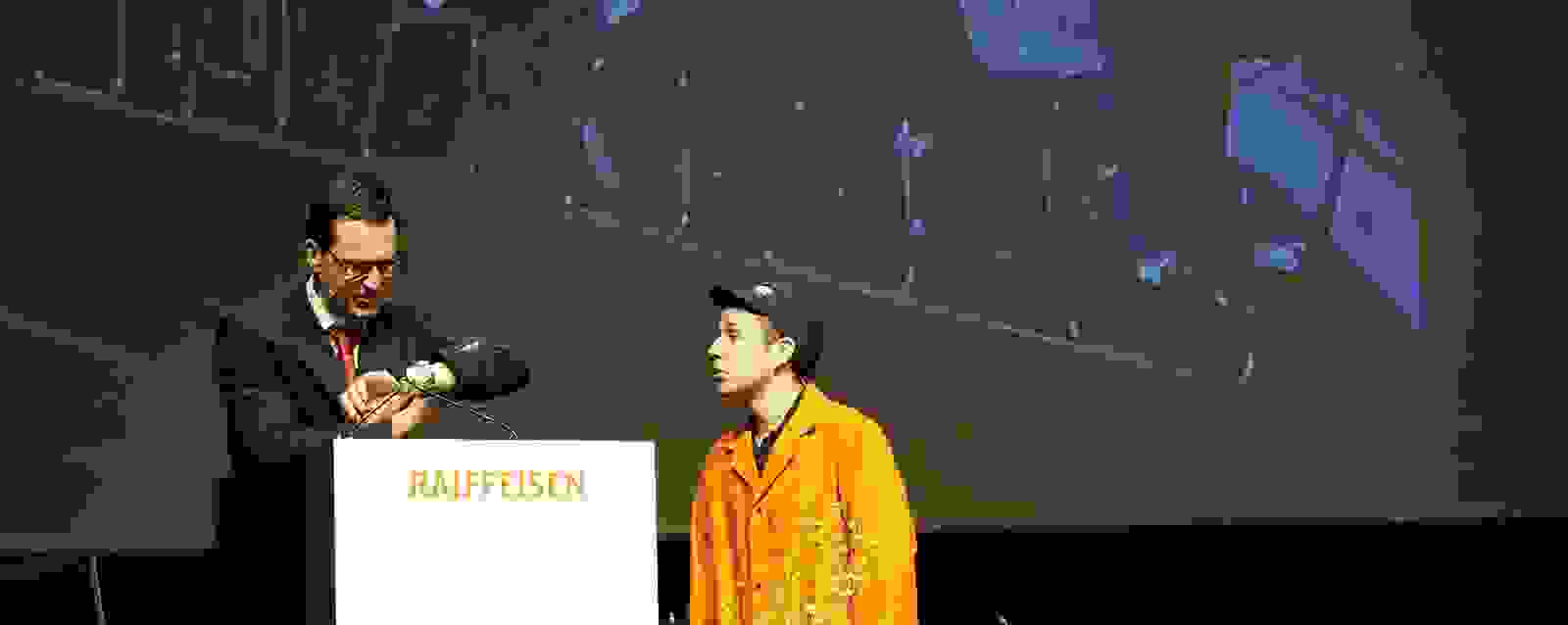 Komiker auf dem Podium während Generalversammlung einer Raiffeisenbank. 