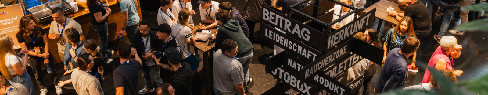Menschen an einem Mitarbeitendenanlass, in der Mitte steht ein Wegweiser, wo welche Räume in der Location sind. 
