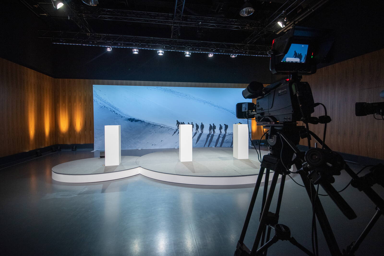 Digitale Mitarbeiterinformation Podium mit grosser Leinwand im Hintergrund. Vordergrund steht eine Kamera, die die digitale Mitarbeiterinformation aufzeichnet.