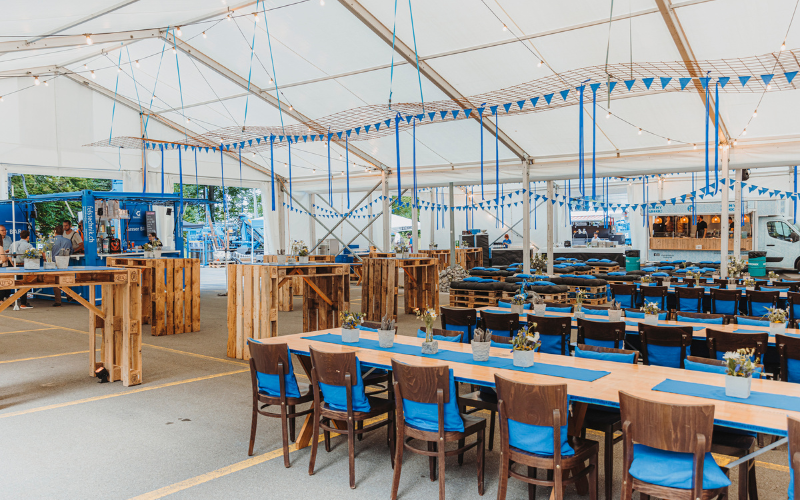 Mitarbeiteranlass zum 100 Jahre Jubiläum  Festlich dekoriertes Zelt mit Tischen, Stehtischen, Sofas in der Firmenfarbe blau.