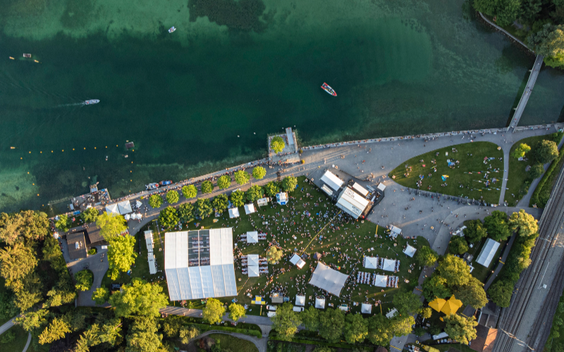 Drohnenaufnahme von einem Festivalgelände mit Zelten am See. 