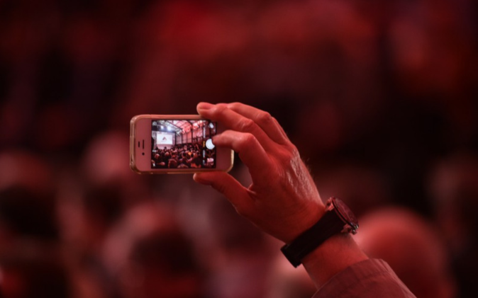 Eröffnungsfest Gotthard-Basistunnel Eine Hand mit Handy, auf Bildschirm werden Feierlichkeiten aufgezeichnet.