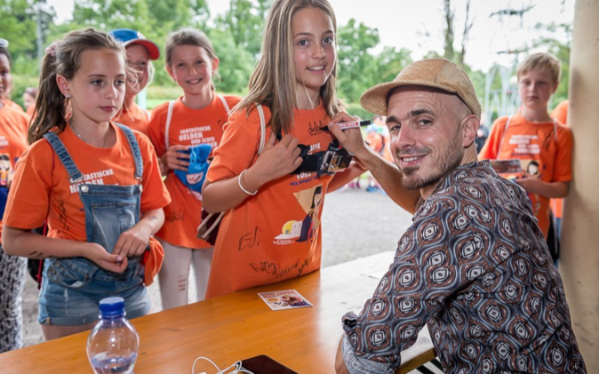 Jugendanlass der Raiffeisen Schweiz DODO unterschreibt ein Tshirt eines Kindes.