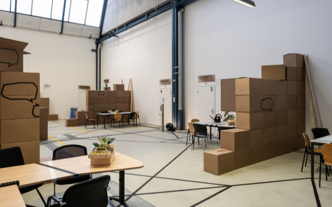 Eingerichteter Co-Working-Space mit Wänden aus Kartonschachteln, Tischen und Stühlen