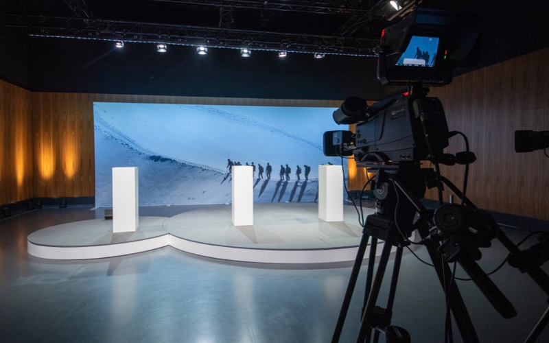 Bühne mit Podium und Hintergrundbild, vorne Kamera für die Übertragung einer Informationsveranstaltung für Mitarbeitende