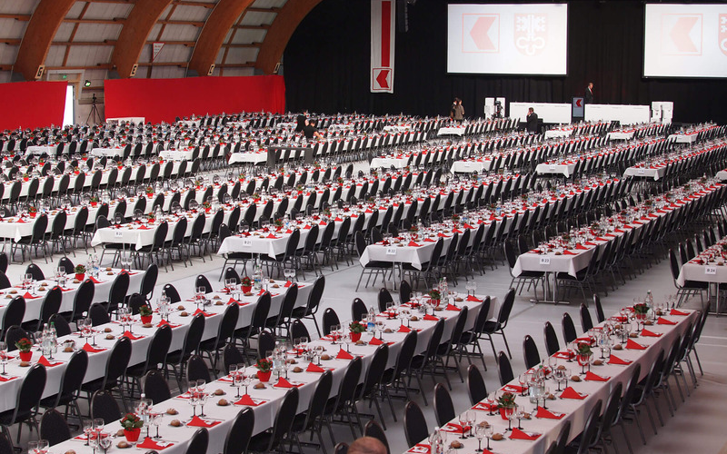 Partizipations-Versammlung der Nidwaldner Kantonalbank Halle mit vielen schön gedckten Tischen und Stühlen. Farben rot und weiss.