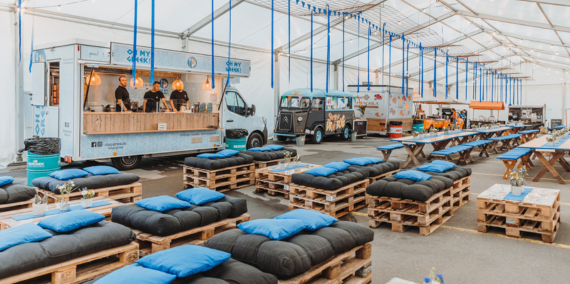 Festlich dekoriertes Zelt mit Tischen, Stehtischen, Sofas in der Firmenfarbe blau. 