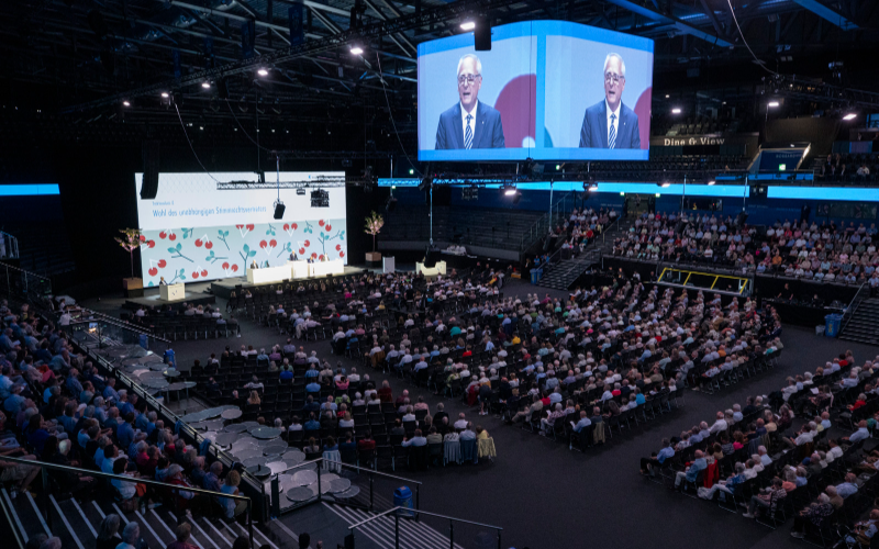 GV-Saal während GV, viele Aktionär*innen und zwei Leinwände. 