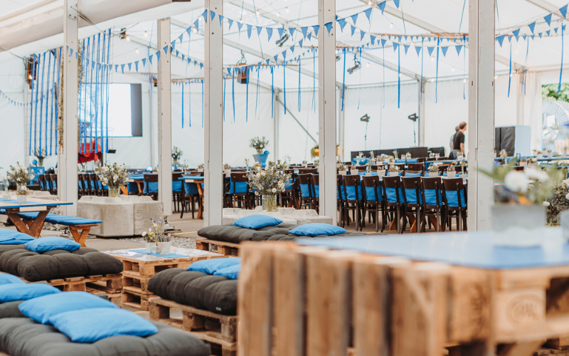 Mitarbeiteranlass zum 100 Jahre Jubiläum  Festlich dekoriertes Zelt mit Tischen, Stehtischen, Sofas in der Firmenfarbe blau.