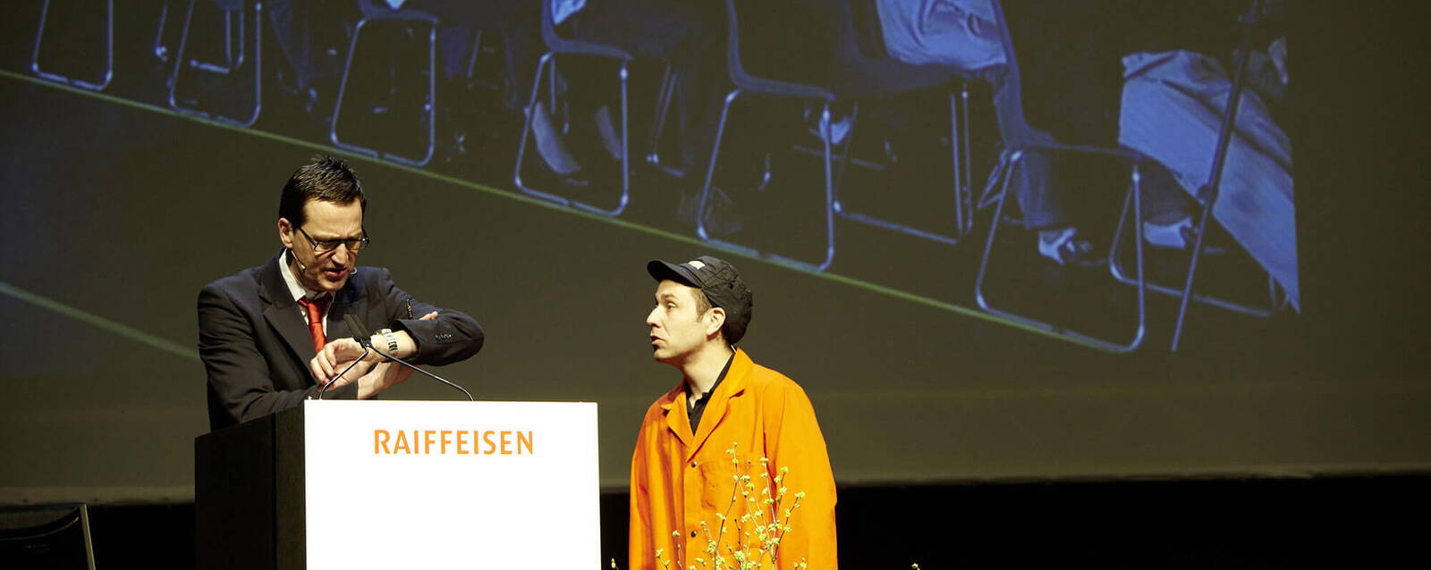 Komiker auf dem Podium während Generalversammlung einer Raiffeisenbank. 