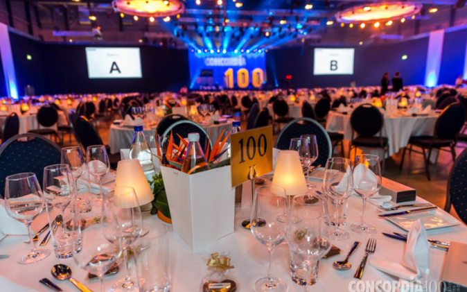 Mitarbeiterfeier zum 100-jährigen Jubiläum der Concordia Feierlich gedeckte Tische, Hintergrund Leinwand und Bühne. Keine Personen.