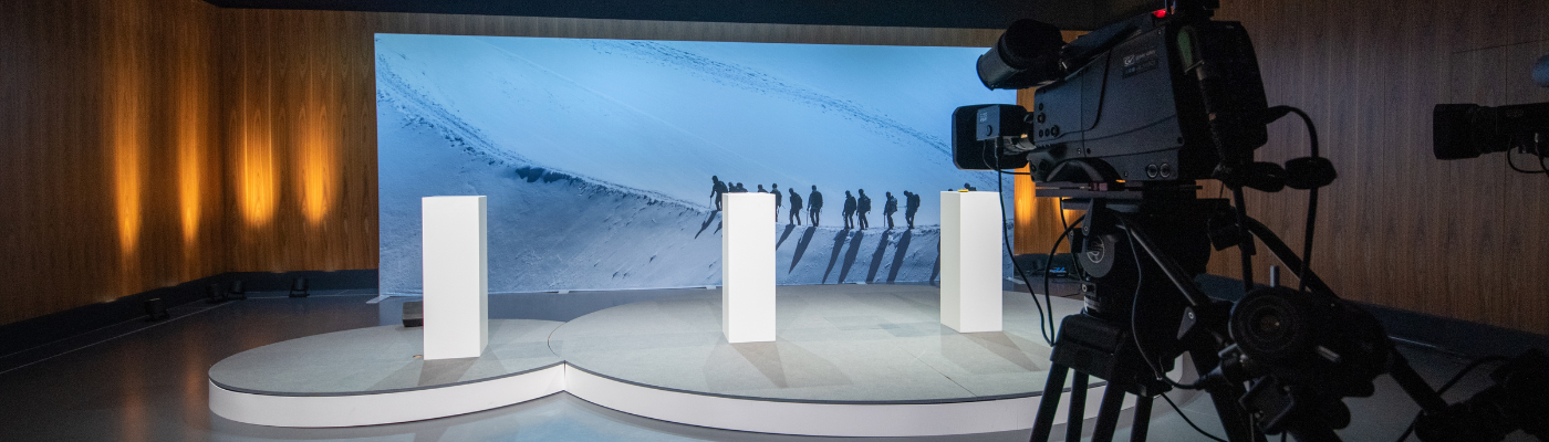 Digitale GV Bühne mit Rednerpult und Hintergrundbild, im Vordergrung eine Kamera, die ganze Bühne filmt für einen digitalen Event.