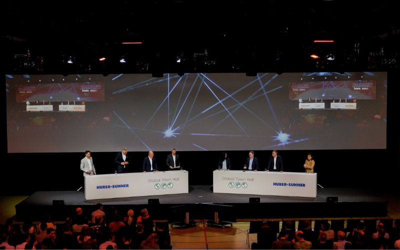 Global Town Hall Huber + Suhner AG Podium mit 8 Personen am Global Town Hall