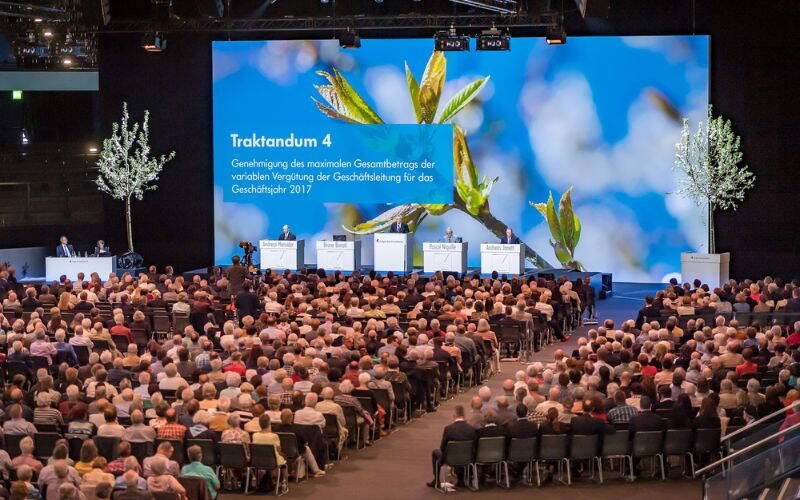 Gäste und grosse Leinwand mit Podium in der Bossard Arena in Zug. 