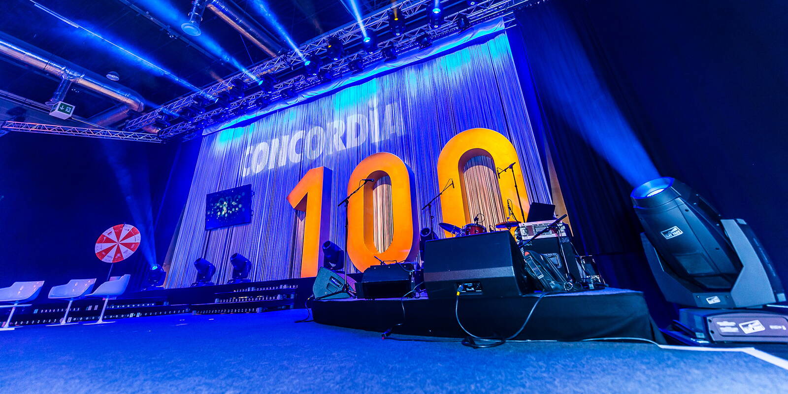 Mitarbeiterfeier zum 100-jährigen Jubiläum der Concordia Bühne mit Logo-Projektion und Nummer 100. Im Vordergrund die Instrumente der Band.