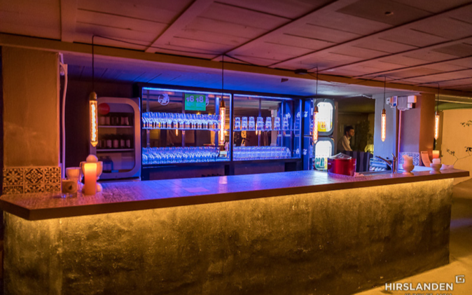 Mitarbeiterfest mit Vintage-Charme Bartrese mit beleuchtetem Barelement im Hintergrund.